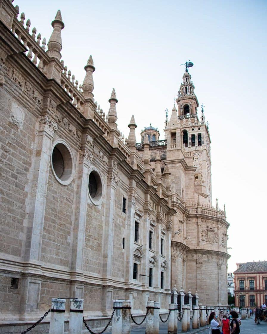 Seville's Giralda lit up at night, seen from the Avenida de la Constitución, with a line of nazarenos passing in the foreground