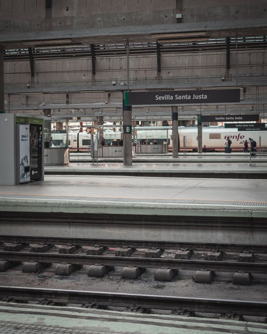 Andén de la estación de Sevilla Santa Justa con un tren AVE detenido bajo la gran bóveda de hormigón y viajeros con maletas caminando hacia la salida