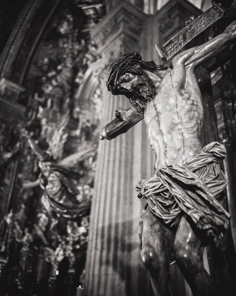 Paso d'un Christ crucifié sur une caisse dorée avançant de nuit dans une rue étroite du centre de Séville, éclairé par des cierges