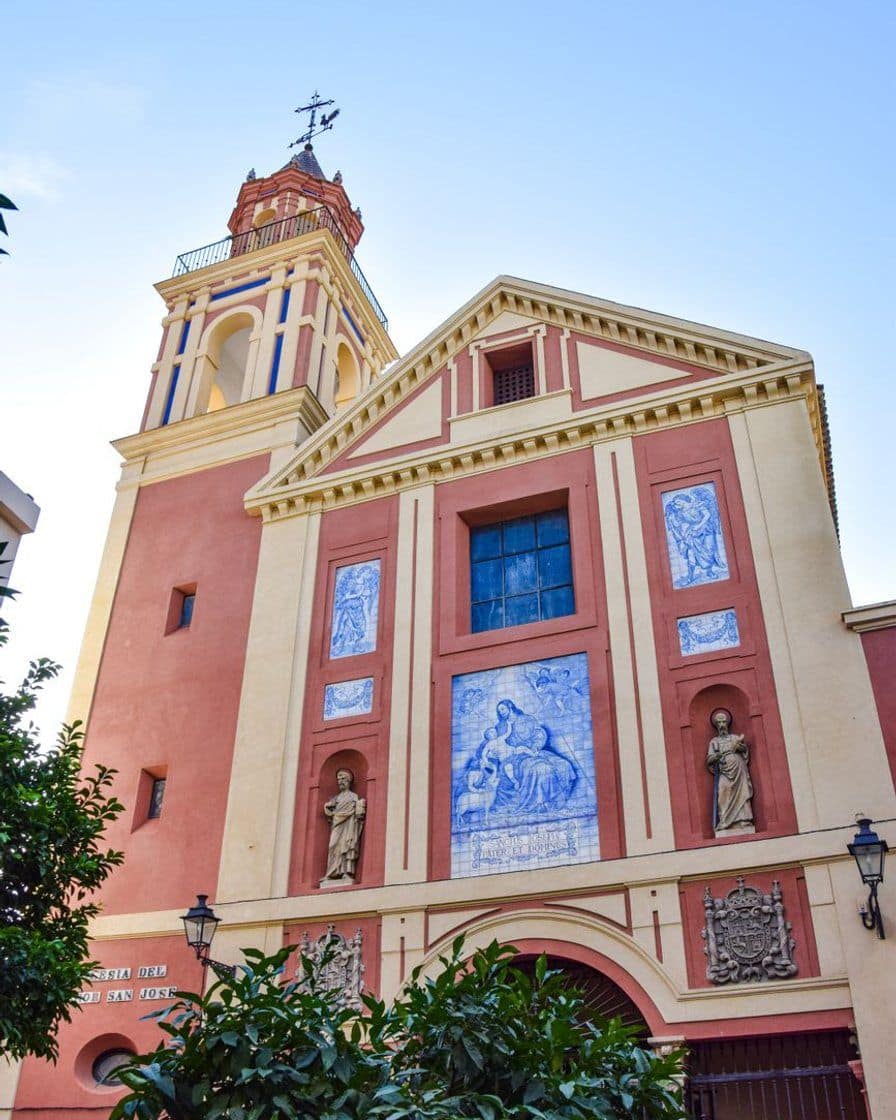 Whitewashed facade of the church of Santa Cruz in Seville with its bell gable and an orange tree in front, mid-morning