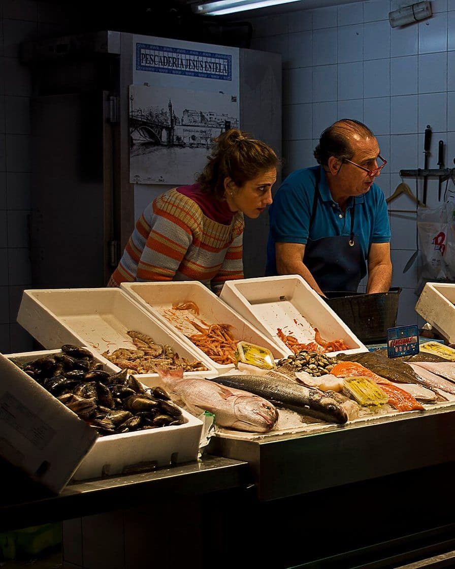 Étals de poisson et de légumes à l'intérieur du marché de Triana à Séville, avec des clients qui font leurs courses le matin