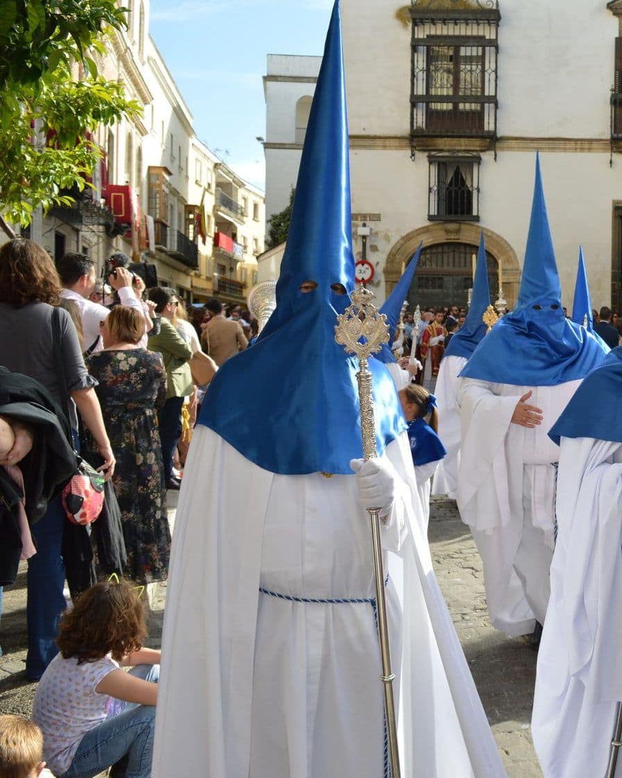 Nazarenos portant des cierges allumés qui avancent au petit matin dans une rue vide de Séville pendant la Madrugá